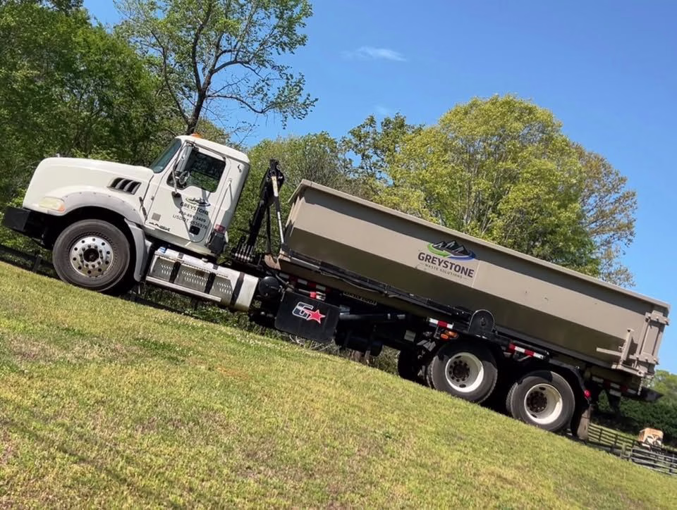 Greystone Waste Solutions roll-off truck in a northwest Georgia field